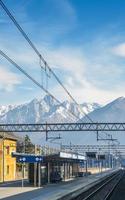 vista dal finestrino esterno del treno presso la piccola stazione ferroviaria e le maestose alpi italiane foto