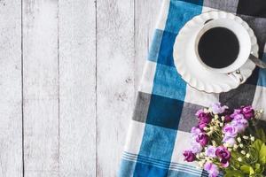 vista dall'alto della tazza di caffè con fiori e tovaglia su sfondo tavolo in legno, spazio libero per testo foto