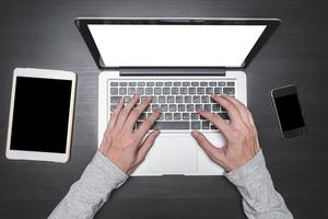vista dall'alto delle mani maschili che lavorano su laptop con tablet e smartphone su sfondo nero scrivania in legno. foto
