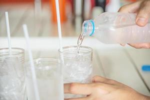 versare a mano acqua fresca in un bicchiere con ghiaccio - concetto di bevanda fredda rinfrescante assetato foto