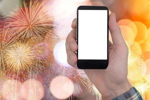 mano maschile che tiene un telefono cellulare con schermo bianco vuoto touch su fuochi d'artificio e sfondo di luci bokeh. foto