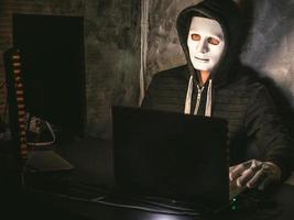 hacker di computer - uomo in maglietta con cappuccio con maschera che ruba i dati dal laptop foto