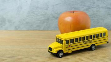 il giocattolo dello scuolabus e la mela sul tavolo di legno per il ritorno a scuola o il concetto di istruzione foto