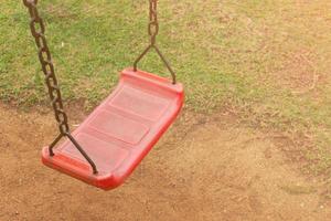 un'altalena rossa è attaccata a una vecchia catena arrugginita nel parco giochi. nel parco ha visto la terra e l'erba foto