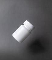 flacone per pillole di plastica bianca, senza etichetta, con tappo, galleggiante su sfondo nero. foto