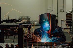 saldatore professionista dell'industria pesante che lavora all'interno della fabbrica, indossa il casco e inizia a saldare. messa a fuoco selettiva foto