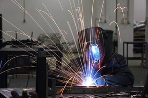 saldatore professionista dell'industria pesante che lavora all'interno della fabbrica, indossa il casco e inizia a saldare. messa a fuoco selettiva foto