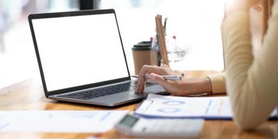 immagine mockup di donna d'affari che usa e digita sul computer portatile con schermo bianco vuoto e tazza di caffè sul tavolo di vetro in un moderno loft cafe foto