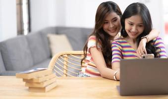 amante delle coppie lesbiche delle giovani belle donne asiatiche che utilizza smartphone e laptop che acquistano online insieme nel soggiorno a casa con la faccia sorridente concetto di sessualità lgbt con uno stile di vita felice insieme. foto