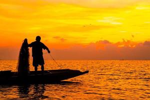 sagoma di pescatori che pescano nel lago all'alba. foto