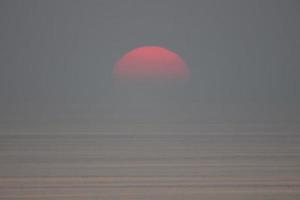 il sole sta cadendo nel mare ed è parzialmente inghiottito dalla nebbia. il cielo è scuro foto