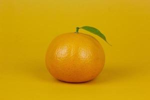 un frutto arancione con foglia verde isolato su sfondo giallo. un frutto arancione con supporto a foglia sul concetto di isolamento per la progettazione di annunci foto