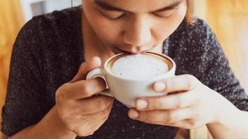 primo piano di una bella ragazza che odora e beve caffè caldo con sentirsi bene al bar si gode il suo cappuccino mattutino con caffè con schiuma di latte foto