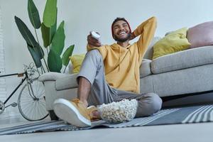 rilassato giovane africano che guarda la tv mentre si siede sul pavimento a casa foto