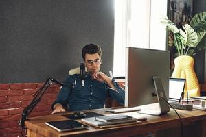 giovane fiducioso che tiene la mano sul mento mentre è seduto all'ufficio della stazione radio foto