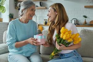 felice madre senior che riceve una confezione regalo e un mazzo di tulipani da sua figlia foto