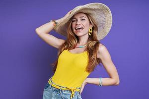 giovane donna attraente che si regola il cappello e sorride mentre si trova su sfondo viola foto