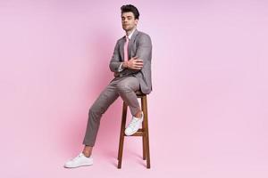 uomo sicuro di sé in completo seduto sulla sedia su sfondo rosa foto