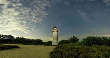 il faro sembra pulito nel mare, il vecchio faro nel deserto. il cielo dietro ha nuvole, stelle e la via lattea. foto