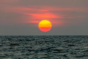 il sole sta cadendo nel mare. , il cielo è arancione e il mare è scuro foto