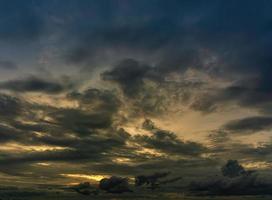 le nuvole riempivano il cielo, oscurando la luce del sole durante il tramonto. il cielo al centro è colorato di arancione dal sole. il cielo inferiore e superiore sono nuvole di pioggia nere e scure. foto