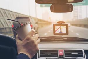 uomo che guida l'auto utilizzando il navigatore e tenendo una tazza di caffè foto