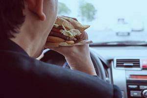 uomo che guida l'auto mentre mangia hamburger foto