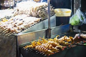 venditore di calamari alla griglia nel cibo di strada locale in yaowarat road famoso luogo turistico tailandia foto