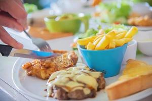 primo piano di persone che mangiano bistecca con salsiccia patatine fritte e piatto di insalata - persone con concetto di fast food foto