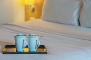 primo piano della tazza di caffè di benvenuto doppia sul letto bianco nella camera d'albergo - concetto di viaggio di vacanza di ospitalità dell'hotel foto