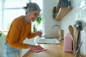 donna anziana fiduciosa che riordina il bancone della cucina e sorride foto