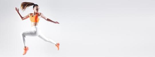 giovane donna sicura di sé in abbigliamento sportivo che salta su sfondo bianco foto