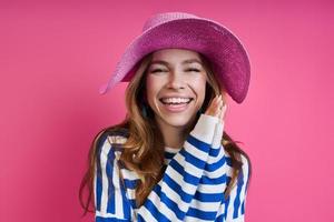 attraente giovane donna in cappello rosa sorridente mentre in piedi su sfondo colorato foto