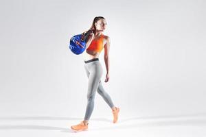 giovane donna in abbigliamento sportivo che porta una borsa mentre si cammina su sfondo bianco foto
