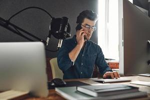 bel giovane che parla al cellulare mentre è seduto all'ufficio della stazione radio foto