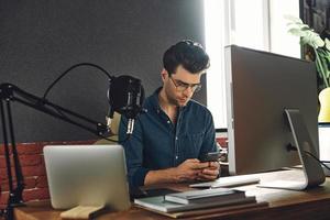 giovane fiducioso che usa lo smartphone mentre è seduto all'ufficio della stazione radio foto