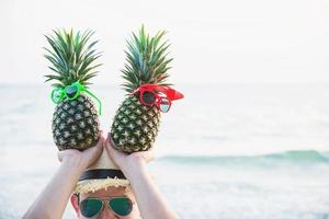 bella coppia ananas fresco mettendo occhiali ragazzo e ragazza nelle mani turistiche con sfondo onda del mare - buon divertimento con un sano concetto di vacanza foto