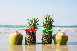 cocco fresco e ananas mettono occhiali da sole incantevoli sulla spiaggia di sabbia pulita con sfondo onda del mare - frutta fresca con concetto di sfondo vacanza sole di sabbia di mare foto