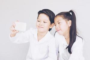 adorabili ragazzi della scuola delle coppie asiatiche stanno prendendo selfie, 7 e 10 anni, su sfondo grigio foto