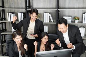 uomini d'affari felici al computer che celebrano il successo sul lavoro seduti in un ufficio moderno. trattative di successo. squadra di affari che esamina il monitor del computer. foto