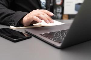 organizzare il processo di lavoro nel proprio blocco note gustando un gustoso cappuccino seduto al chiuso al computer portatile. lavorando sulla scrivania con laptop e smartphone. foto