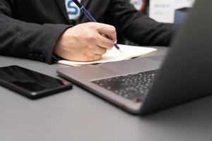 organizzare il processo di lavoro nel proprio blocco note gustando un gustoso cappuccino seduto al chiuso al computer portatile. lavorando sulla scrivania con laptop e smartphone. foto