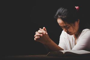 la mano della donna cristiana sulla Bibbia è pregare e adorare per ringraziare dio in chiesa con sfondo nero, concetto di fede, spiritualità e religione foto