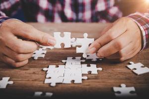 mani che tengono il pezzo di puzzle sul fondo della tavola di legno, affari di successo, strategia di soluzione, concetto di partenariato di lavoro di squadra foto