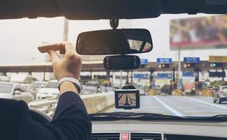 uomo che guida l'auto utilizzando il navigatore e tenendo il dispositivo elettronico del sistema di riscossione dei pedaggi foto