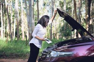 donna asiatica che chiama il riparatore o il personale assicurativo per risolvere un problema al motore di un'auto su una strada locale - persone con problemi di trasporto dell'auto concetto foto