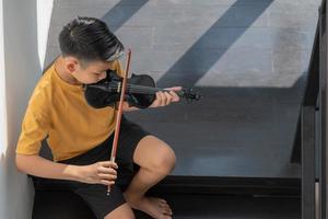 un ragazzino asiatico che suona e pratica lo strumento a corda musicale del violino contro in casa, concetto di educazione musicale, ispirazione, studente di scuola d'arte per adolescenti. foto