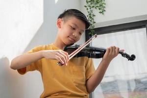 un ragazzino asiatico che suona e pratica lo strumento a corda musicale del violino contro in casa, concetto di educazione musicale, ispirazione, studente di scuola d'arte per adolescenti. foto