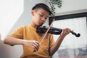 un ragazzino asiatico che suona e pratica lo strumento a corda musicale del violino contro in casa, concetto di educazione musicale, ispirazione, studente di scuola d'arte per adolescenti. foto