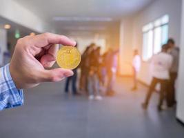 primo piano della mano dell'uomo che tiene una moneta bitcoin con lo sfondo dell'ufficio foto